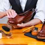 by dimamorgan12 from Getty Images close up of shoe professional shining a pair of men's tan shoes with Brush and polish on table