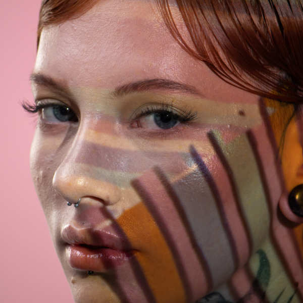 Close up image of a young women holding a transparent color palette with light showing through to  her face to see which color shade is complimentary