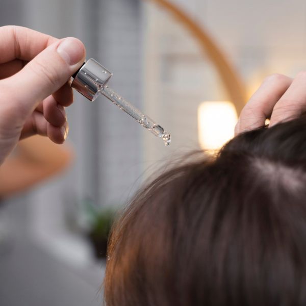 Hair Treatment 2_ by Dali Images Close up image of the top of a women's dark brown hair at the part with the hand of a stylist and eyedropper apply treatment
