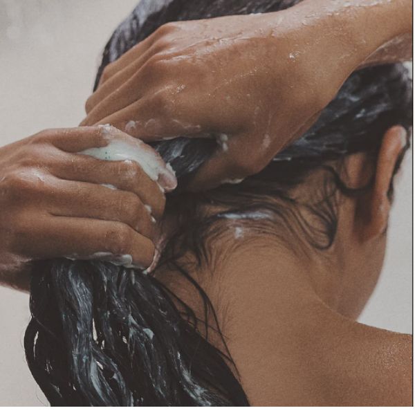 Rear view of young women with long dark brown hair, her hands are carefully shampooing as part of hair care for long hair