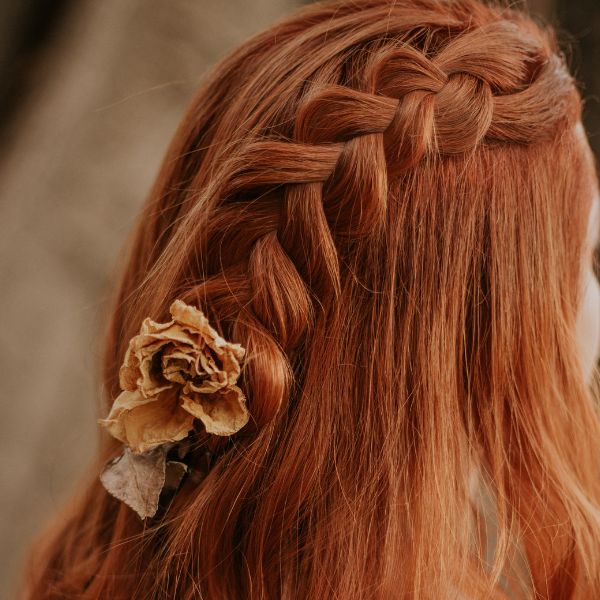Sample of a Bohemian Braided Half-up rear view of women with beautiful red hair with a bohemian-braid and light mauve flower.