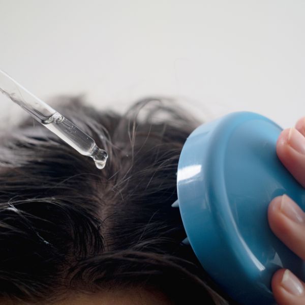 Image showing the top of a customers head in the salon chair with the hands of a stylist applying a treatment oil and combing it through. This is a basic hair conditioning treatment service.