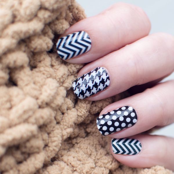 Image of women's fingers on medium beige sweater showing 3 nail art designs on black background and white designs;; geometric, herring-bone, polka dots and si-zag.