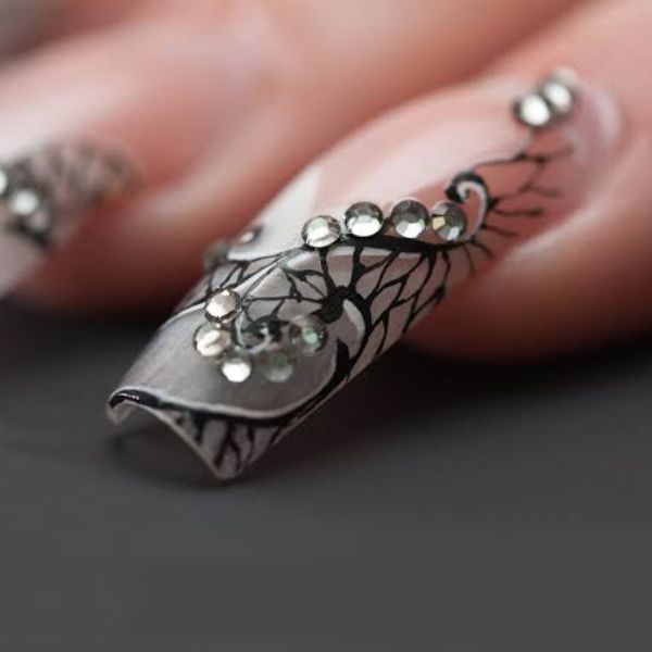 Close up of 3D Nail polish with silver background and various beads glued on for 3D look.