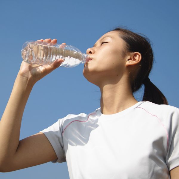 Young women with black hair drinking from a bottle of water to hydrate