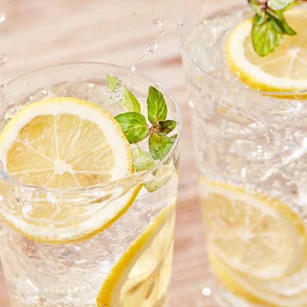 Image of several sliced lemons and a glass of ice water to suggest the importance of hydration for damaged hair