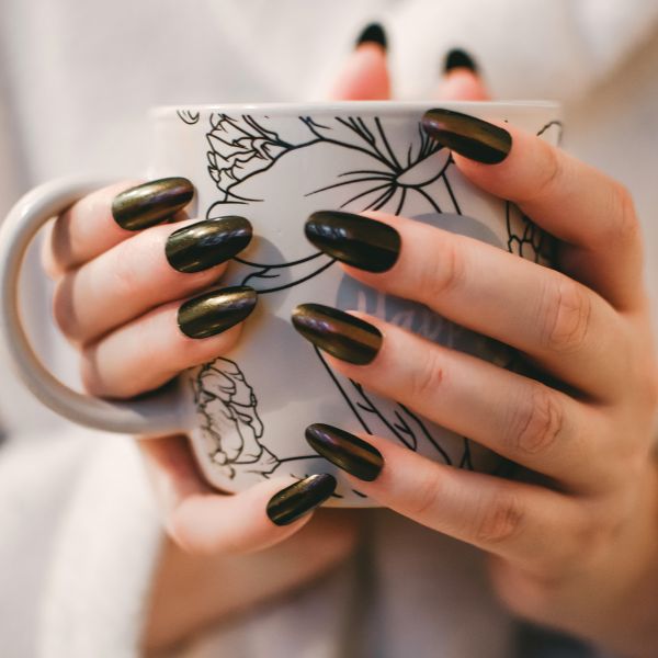 Close up of a women's hand holding a coffee cul with almond shaped nails a trend for stylish nails